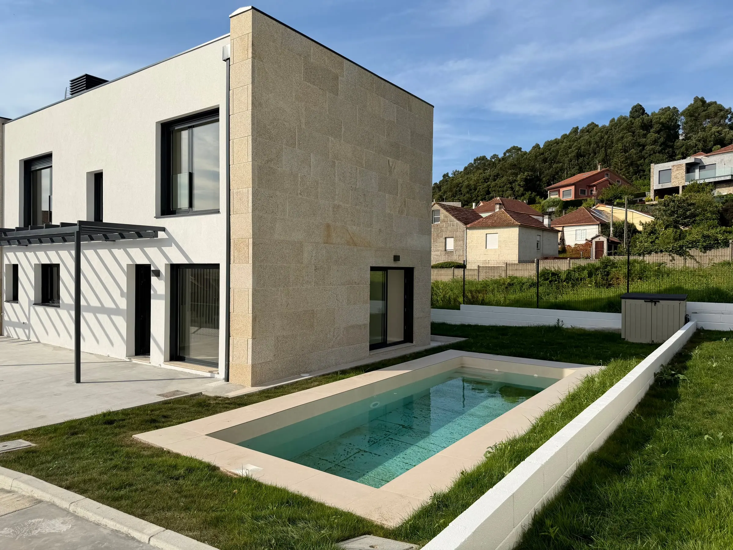 Una de las viviendas de Castrelos terminada: fachada de granito, porche con pérgola y piscina privada